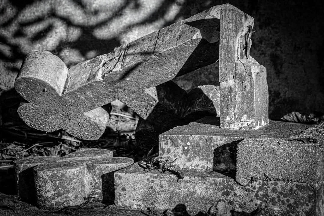 A broken concrete cross lying among cemetery stones.
