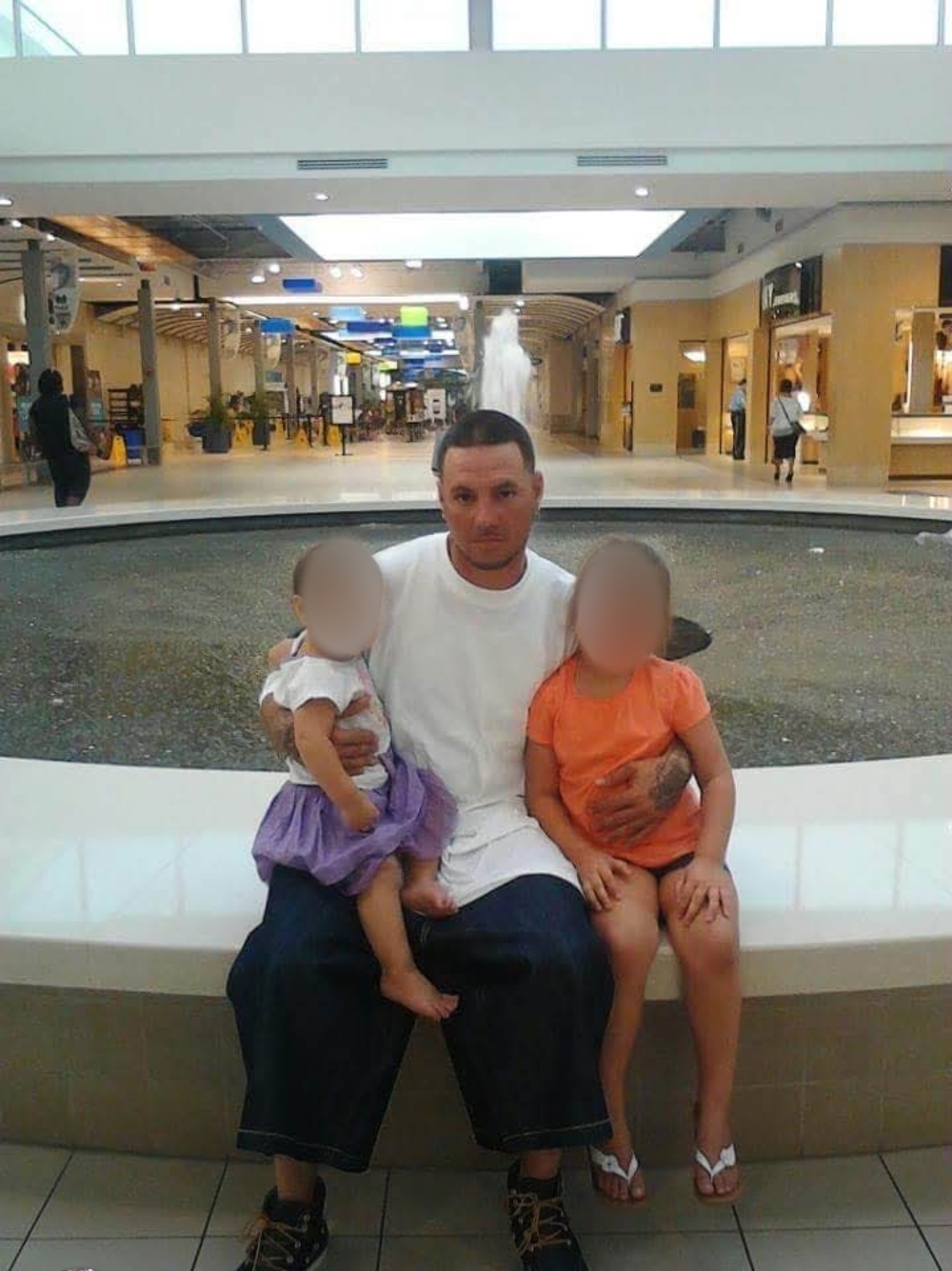 Butch seated with his two young daughters, whose faces are obscured for privacy